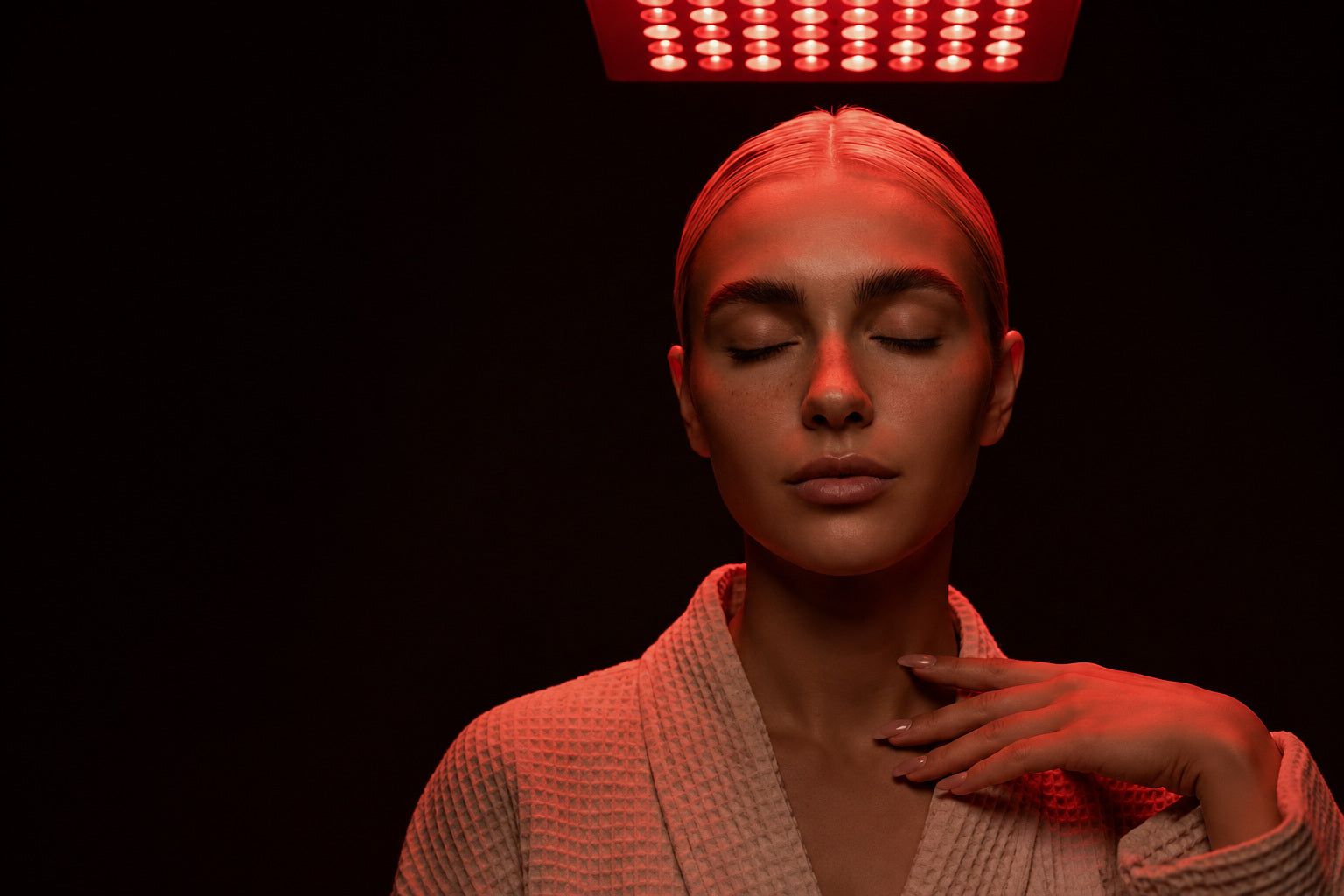 Una mujer con los ojos cerrados bajo un panel LED de luz roja.